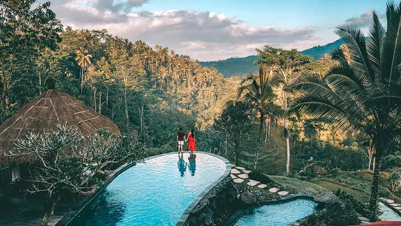 An image of two people standing on the edge of a pool with the stunning nature view, which they found with Visa travel guide.